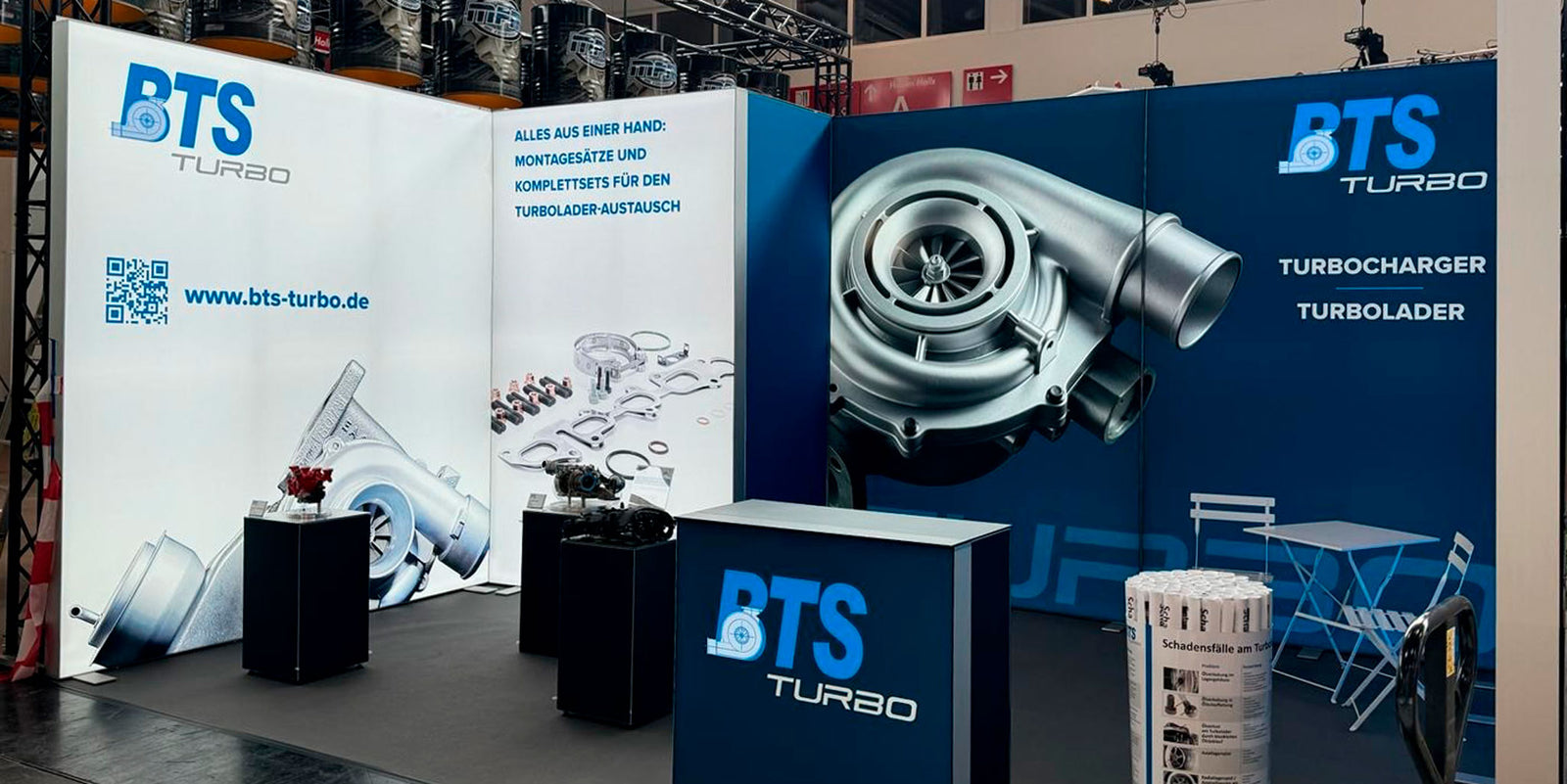 Moderner Messestand von BTS Turbo mit Big LEDUP Textilspannwänden, großformatigen Turbolader-Grafiken, Produktpräsentationen auf Podesten sowie einem Empfangstresen auf einer Fachmesse.