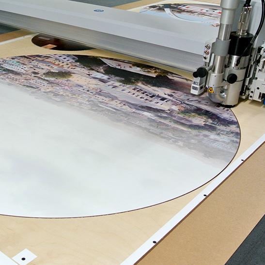 Präziser Zuschnitt eines großformatigen runden Foto-Drucks auf Holz mit einer modernen CNC-Fräse, ideal für Museumsausstellungen und POS-Displays.
