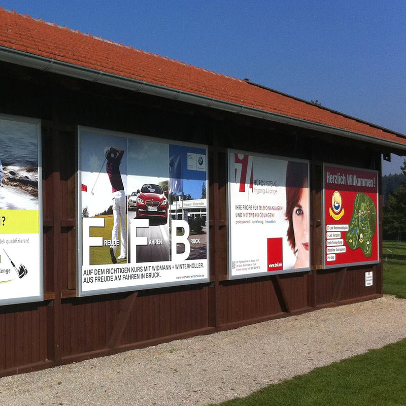 Mehrere Megaframe Wechselrahmen mit bedruckten Planen an einer Holzfassade eines Golfclubs montiert